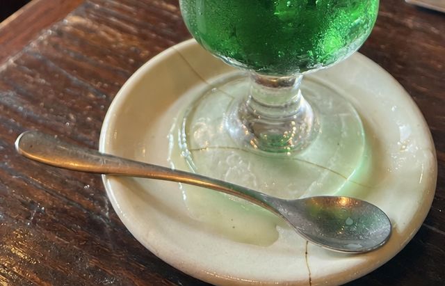 クリームソーダのグラスの足もとに、白い受け皿と銀のスプーン。